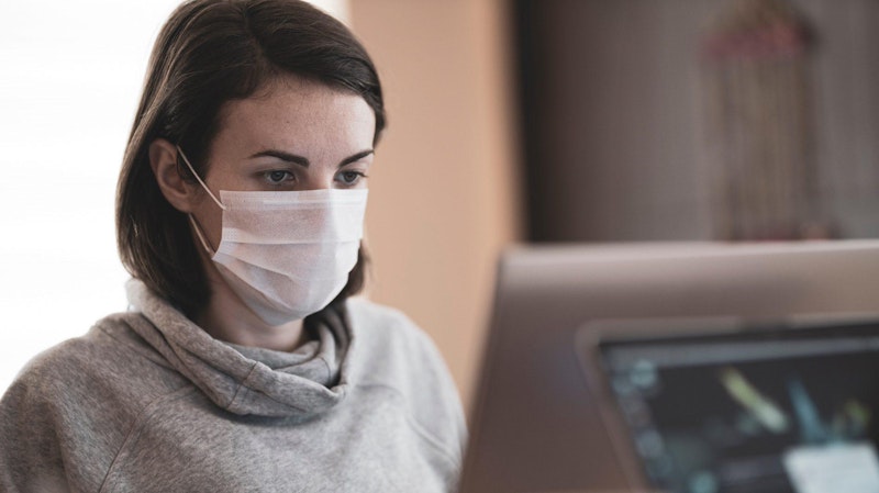 A woman working at a computer and wearing a mask